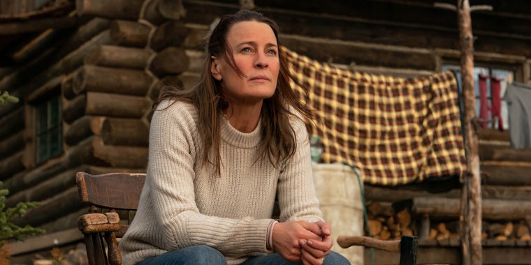 robin wright sits outside a cabin in land