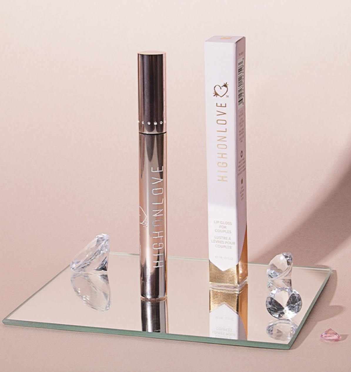 HighOnLove's CBD lip plumping gloss container and packing propped on a mirror next to diamonds.