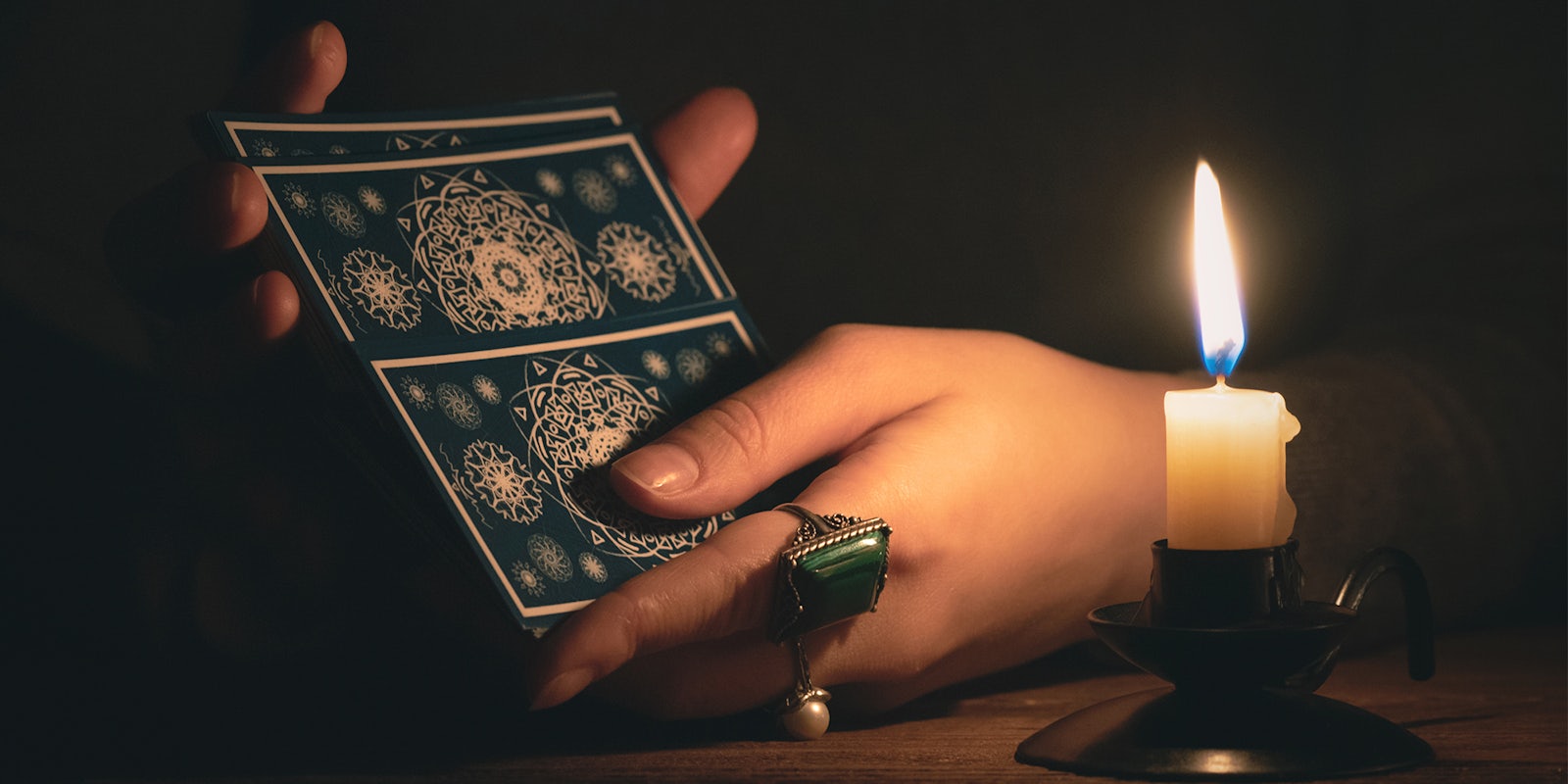 Hands shuffling a tarot deck in candlelight.