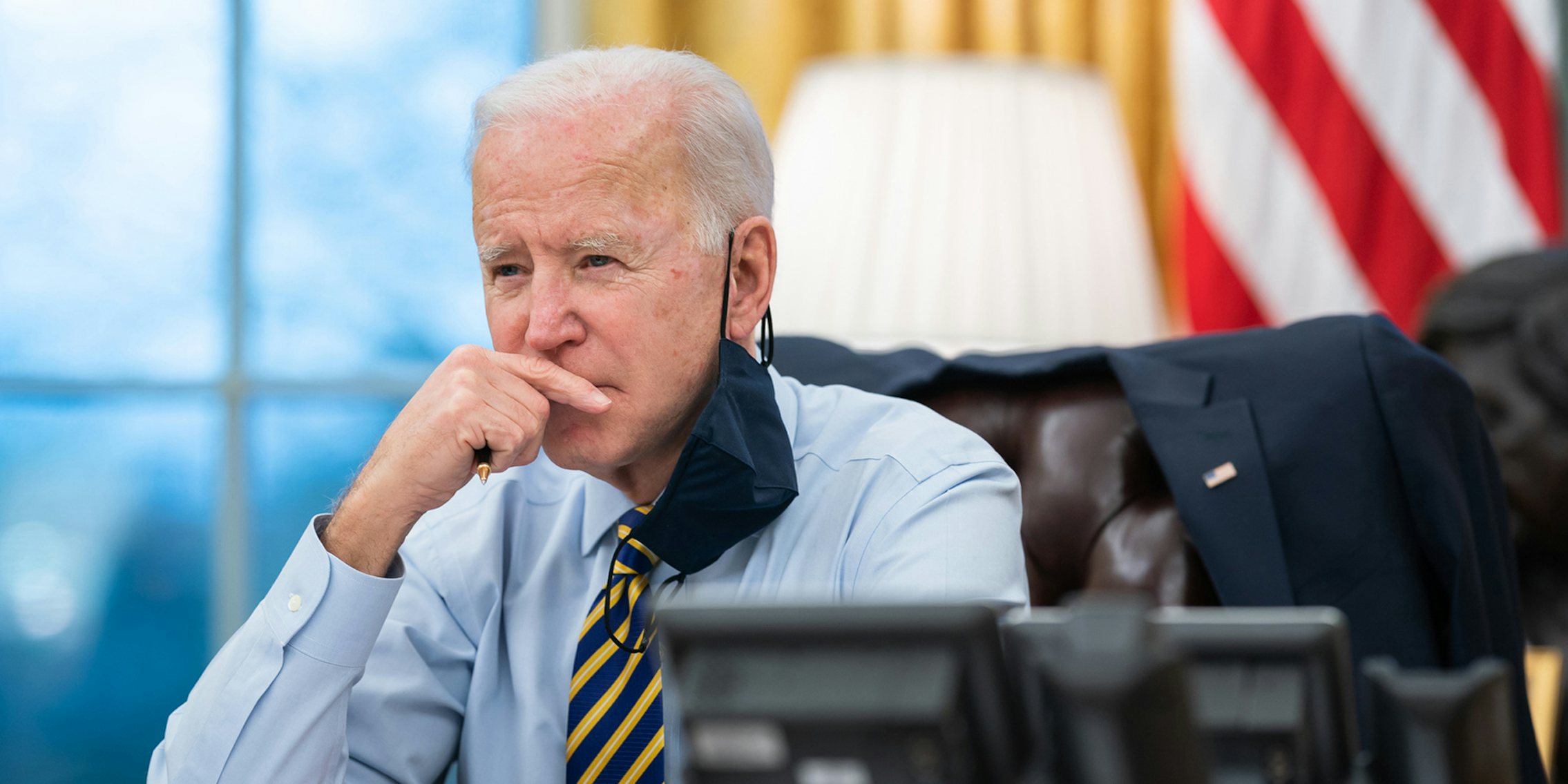 Joe Biden in the Oval Office with his hand up to his face.