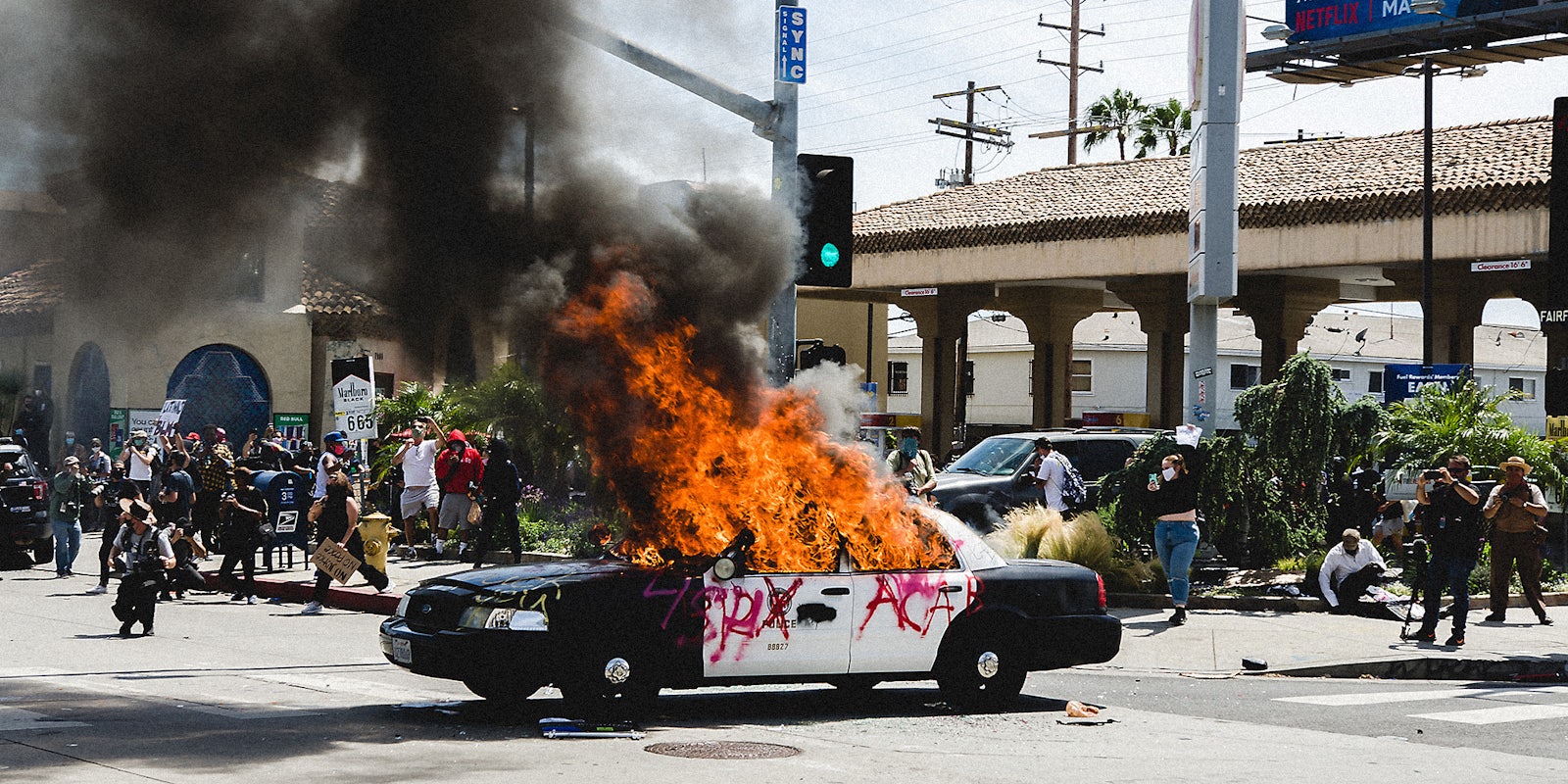 An LAPD car on fire while people watch it burn.