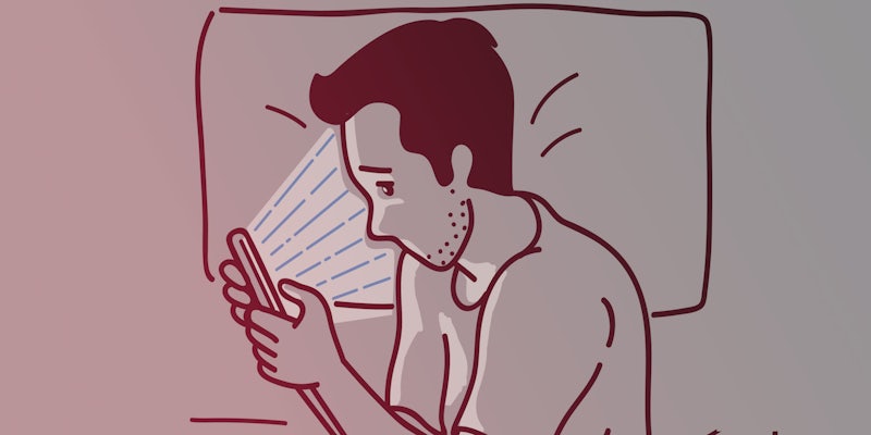 A white man stares at his smartphone in bed