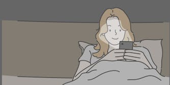 A blonde woman uses a smartphone in bed.