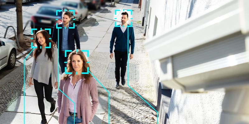 People walking on a sidewalk with a camera using facial recognition to scan them.