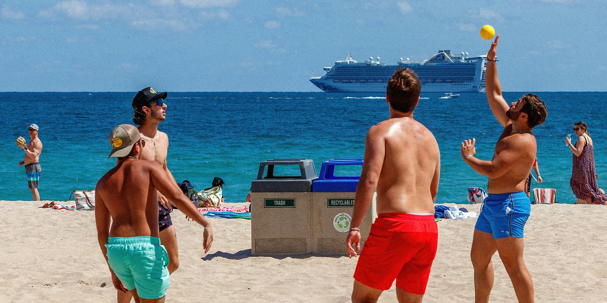 Four college men play with yellow ball on the beach.