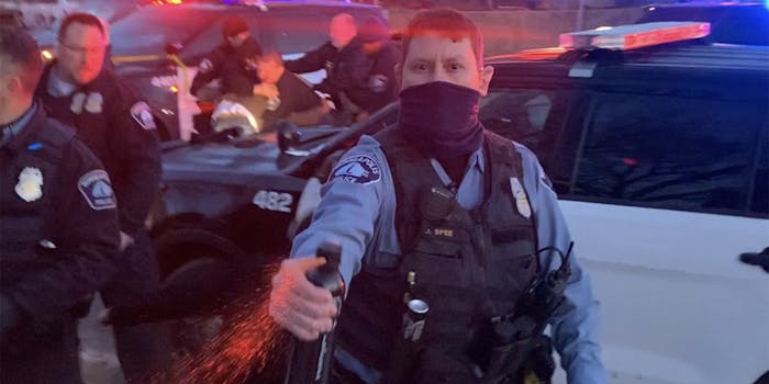 Minneapolis police officer J Spee sprays chemical agent toward camera while officers struggle in the background