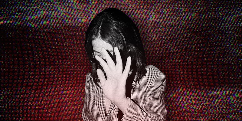 A woman blocks her face from being photographed over a red background.