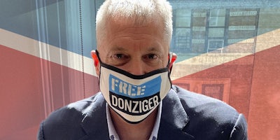 Steven Donziger wearing 'Free Donziger' facemask over Chevron logo background