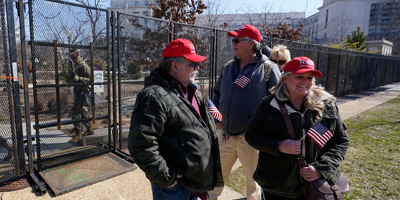 People in Trump caps stand outside fence in Washington DC holding small US flags
