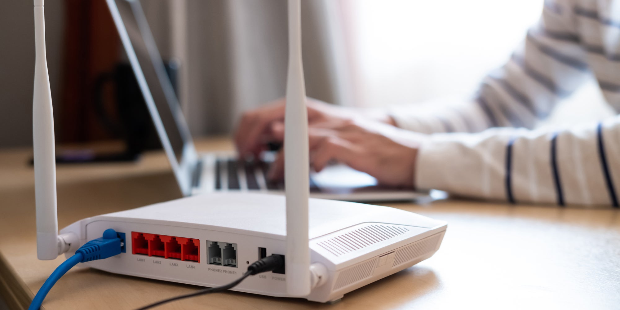 A person typing on a laptop that is connected to broadband internet through a router.