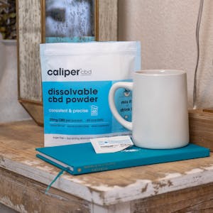 Caliper dissolvable CBD powder next to a coffee mug and book. CBD crytals spilled onto the book.
