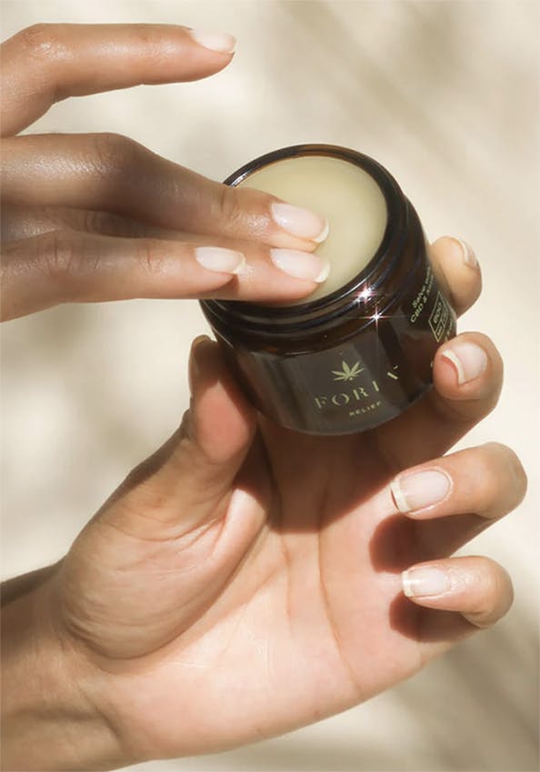 Women dips her fingers into Foria's CBD salve balm with kava.