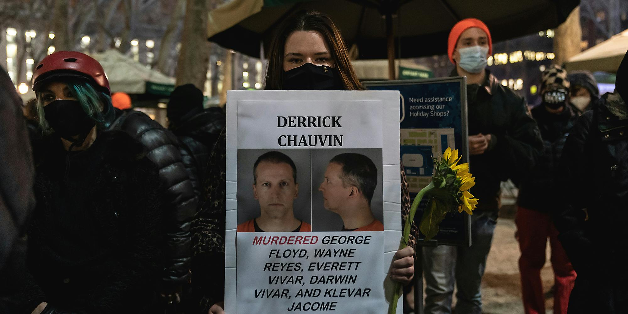 A woman holding a wanted sign for Derek Chauvin.