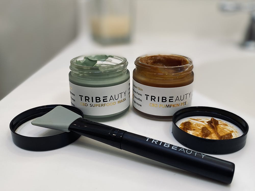 TribeTokes superfood and pumpkin CBD face masks are one of the best stoner gifts for her and him! on the left is a jar of the green superfood mask and on the right is a jar filled with the orange pumpkin mask. in front of it sits a face mask applicator all branded with TRIBETOKES logo.