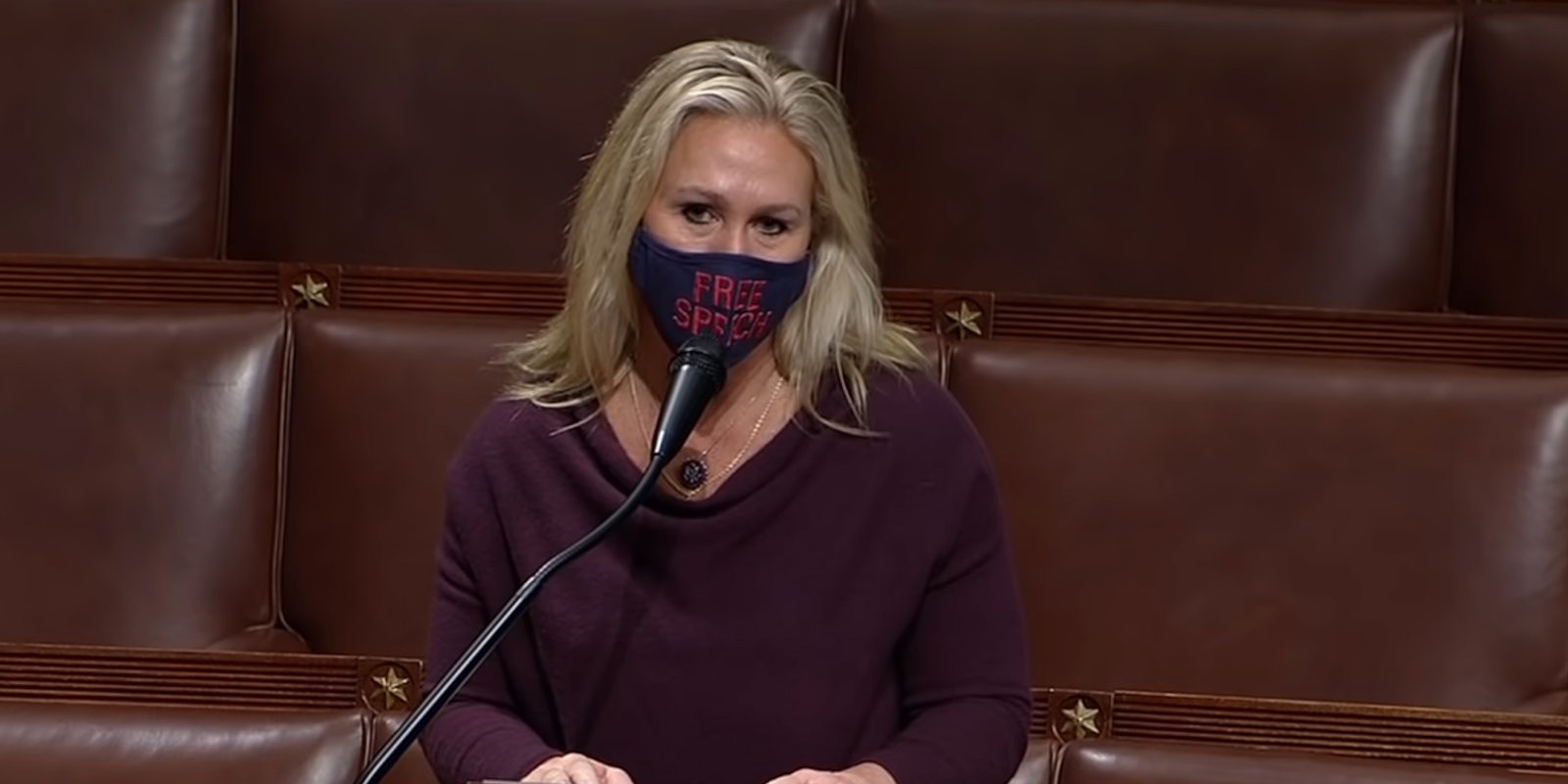 Rep. Marjorie Taylor Greene speaking on the House floor. She is wearing a mask that says 'free speech.'