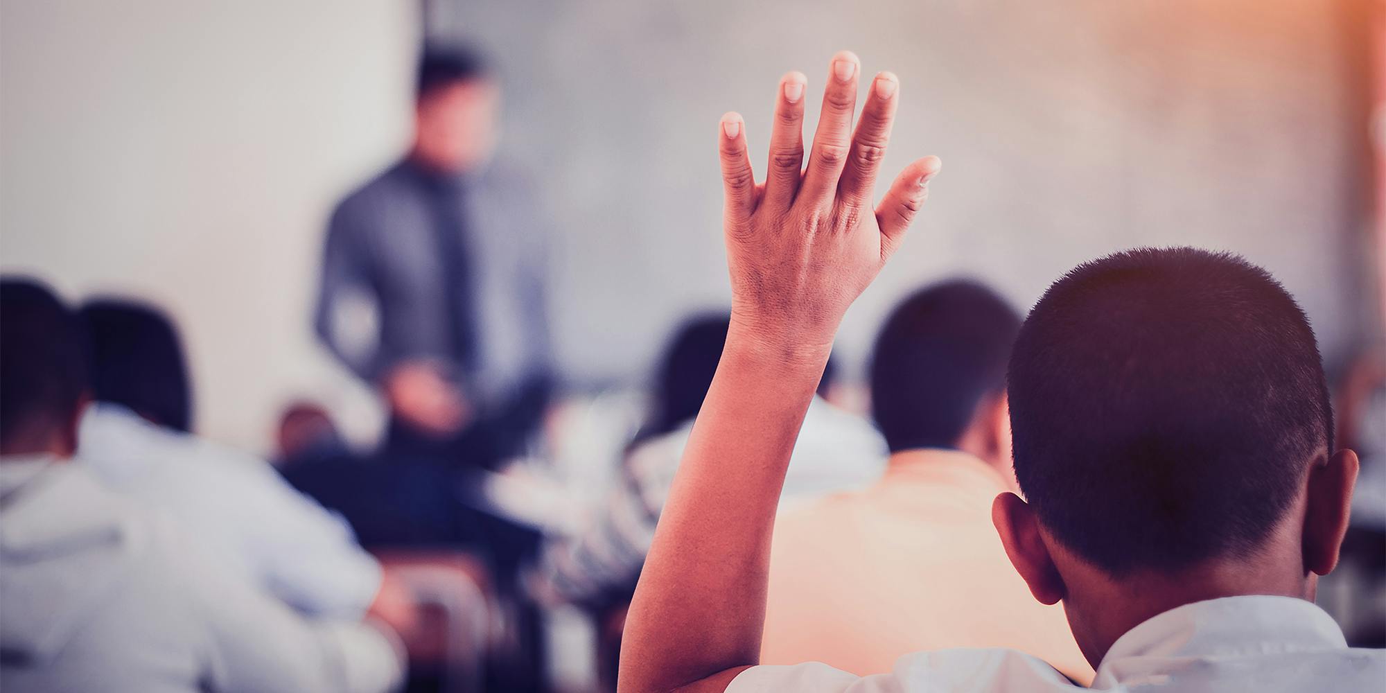 student sitting at their desks and raise their hands in a classroom.