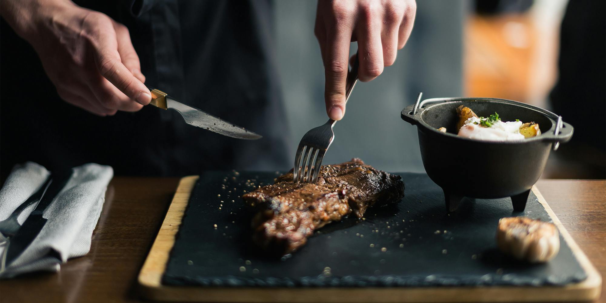 man slicing cooked medium rib eye steak on board