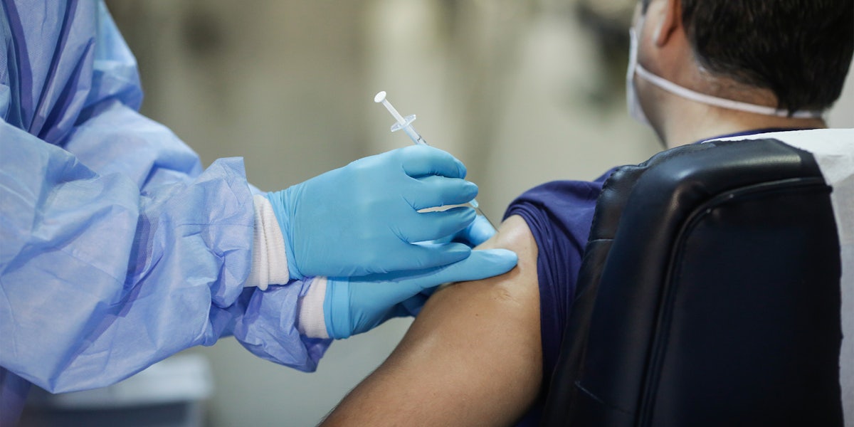 Hands in blue gloves give vaccination to man in mask