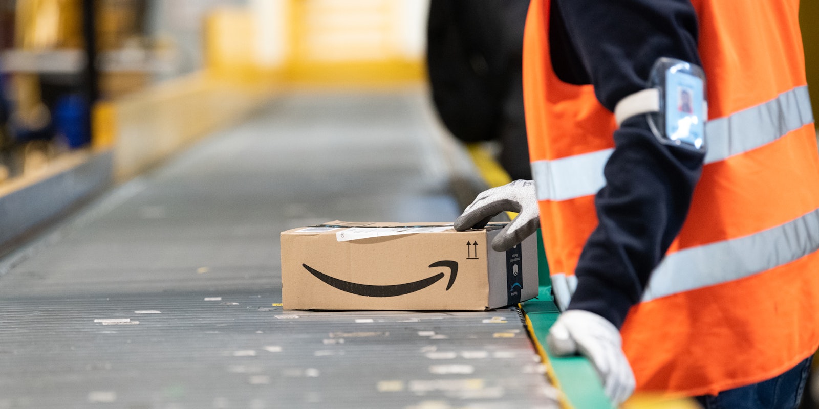An Amazon warehouse worker pushing a package down a conveyer belt.