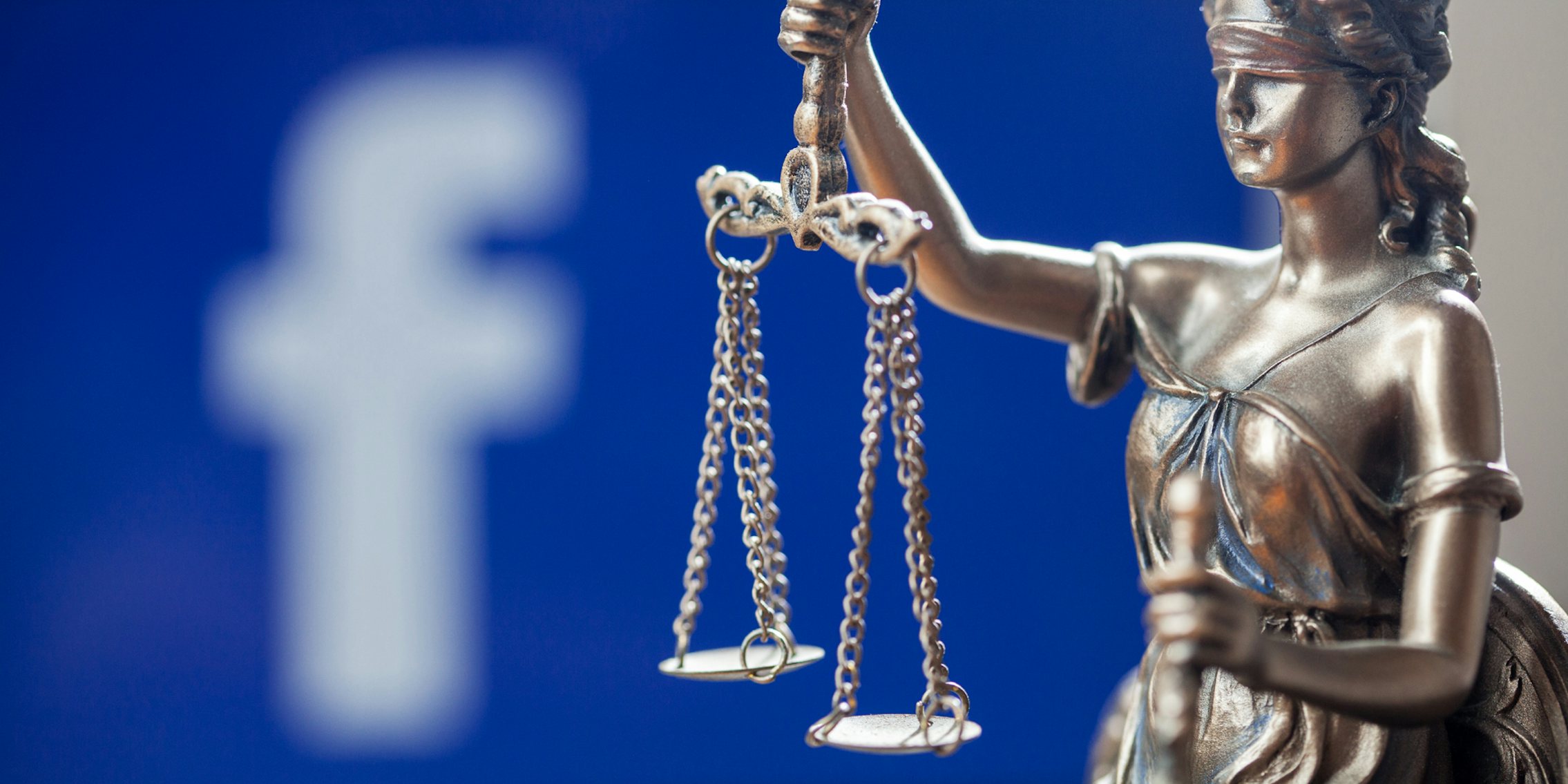 A statue of a woman holding a scale, representing the justice system. Behind the statue is a blurred out Facebook logo.