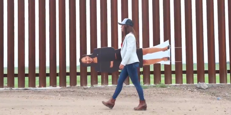 Lauren Boebert walking in front of border fence with cardboard cutout of Kamala Harris