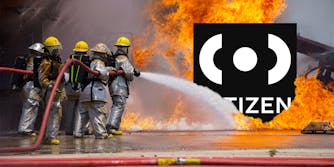 Firefighters hosing down the Citizen app logo, which is engulfed in flames