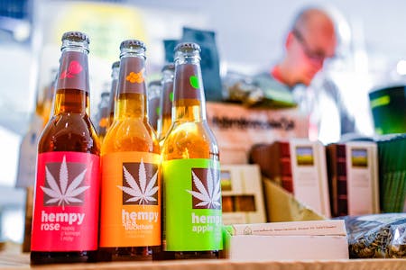 Hemp-based drinks sit in beer style bottles on a store counter with other items for sale in the background which is out of focus