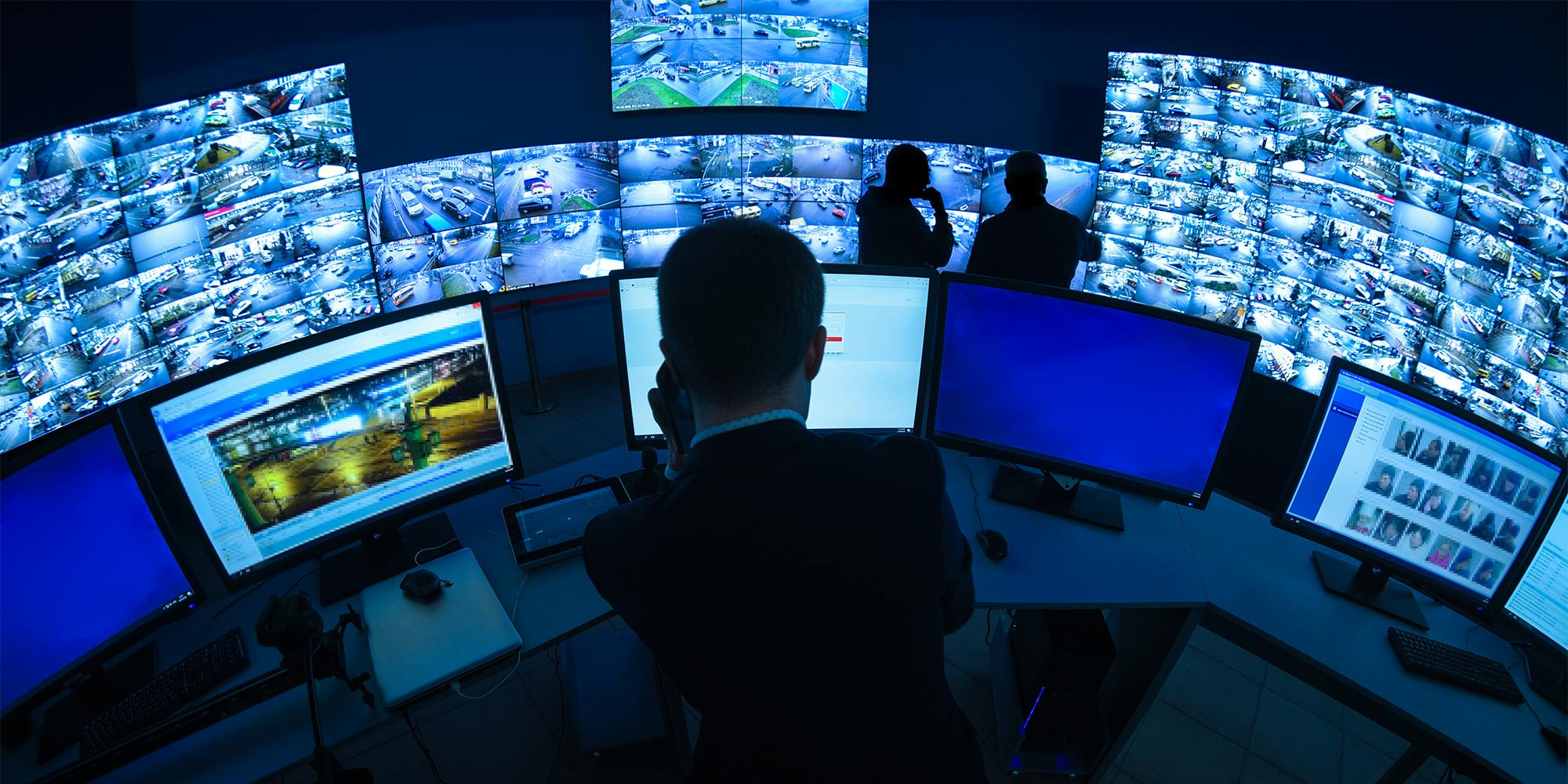A CCTV security room looking at monitors, the cameras show facial recognition being used.