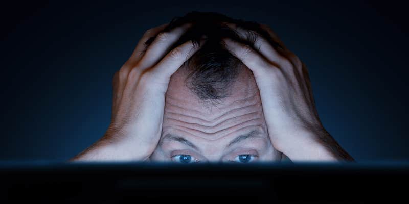 A man with his hands on his head looking frustrated in front of a computer.