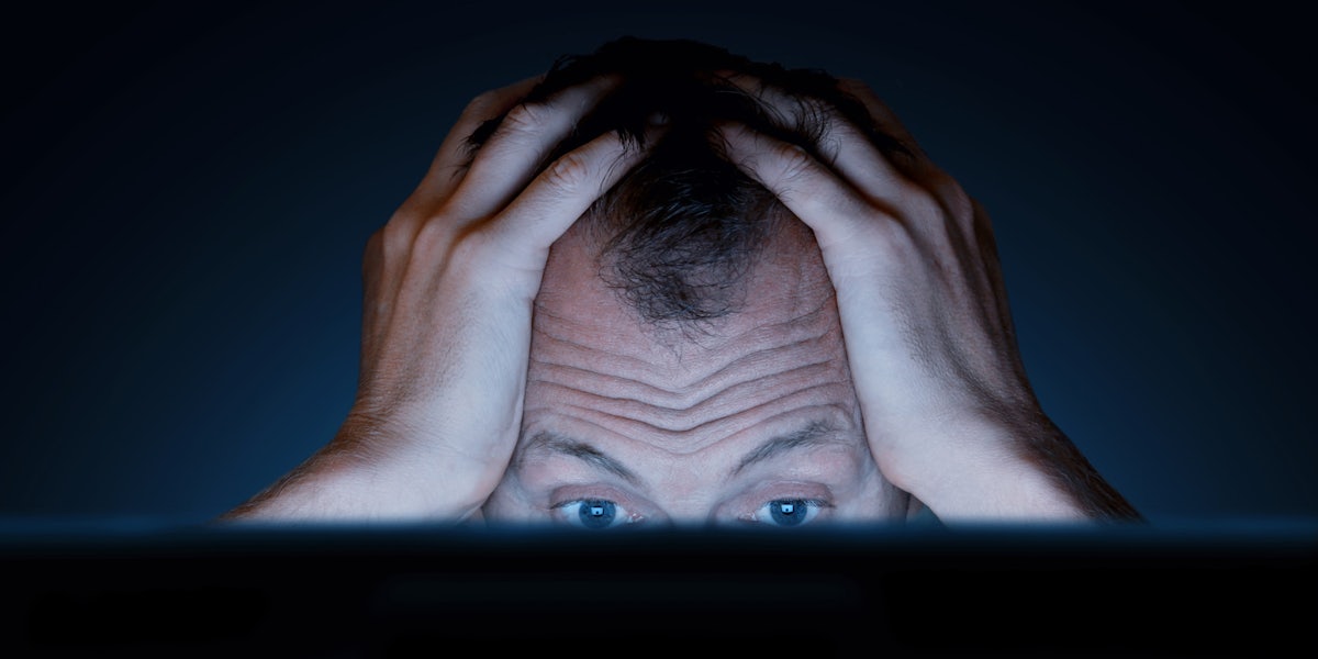 A man with his hands on his head looking frustrated in front of a computer.