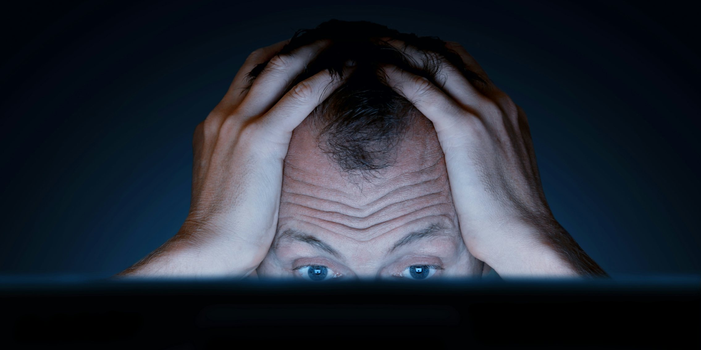 A man with his hands on his head looking frustrated in front of a computer.