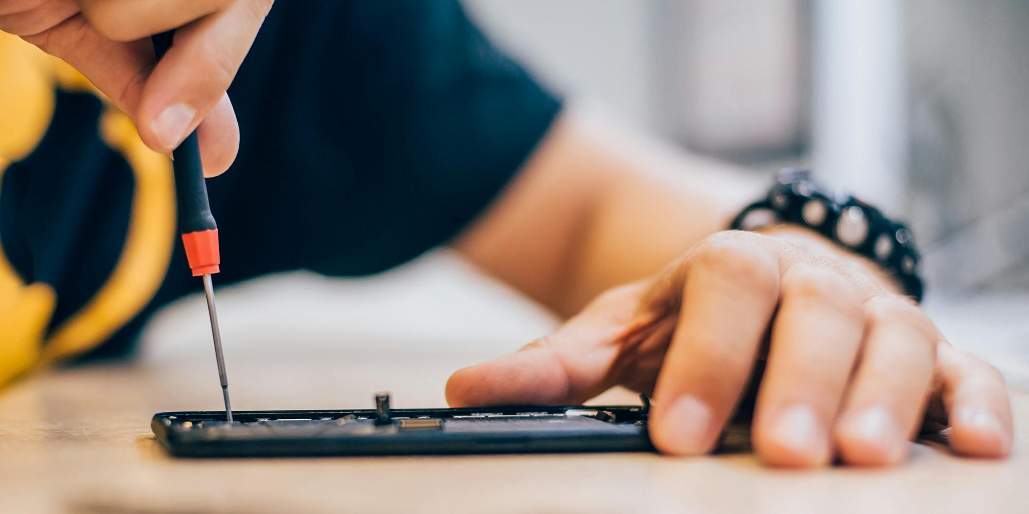 A person holding a smartphone seeking to repair it with a screwdriver.