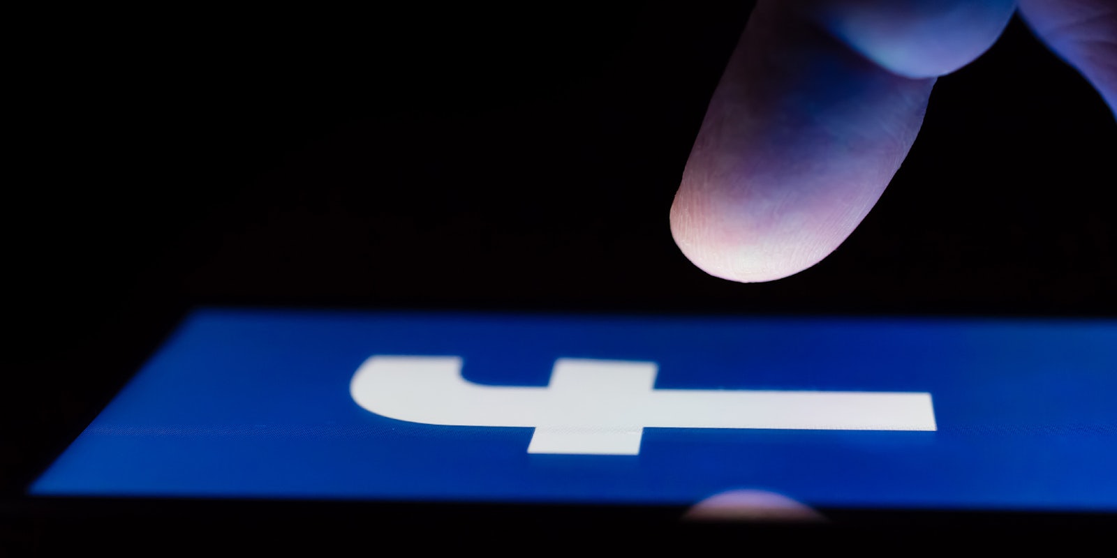 A person touching the Facebook logo on a smartphone in the dark.