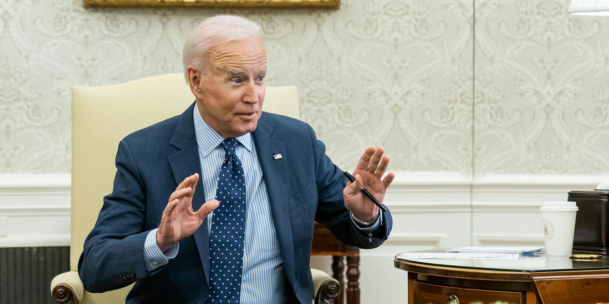 President Joe Biden holding up his arms while sitting in the Oval Office.