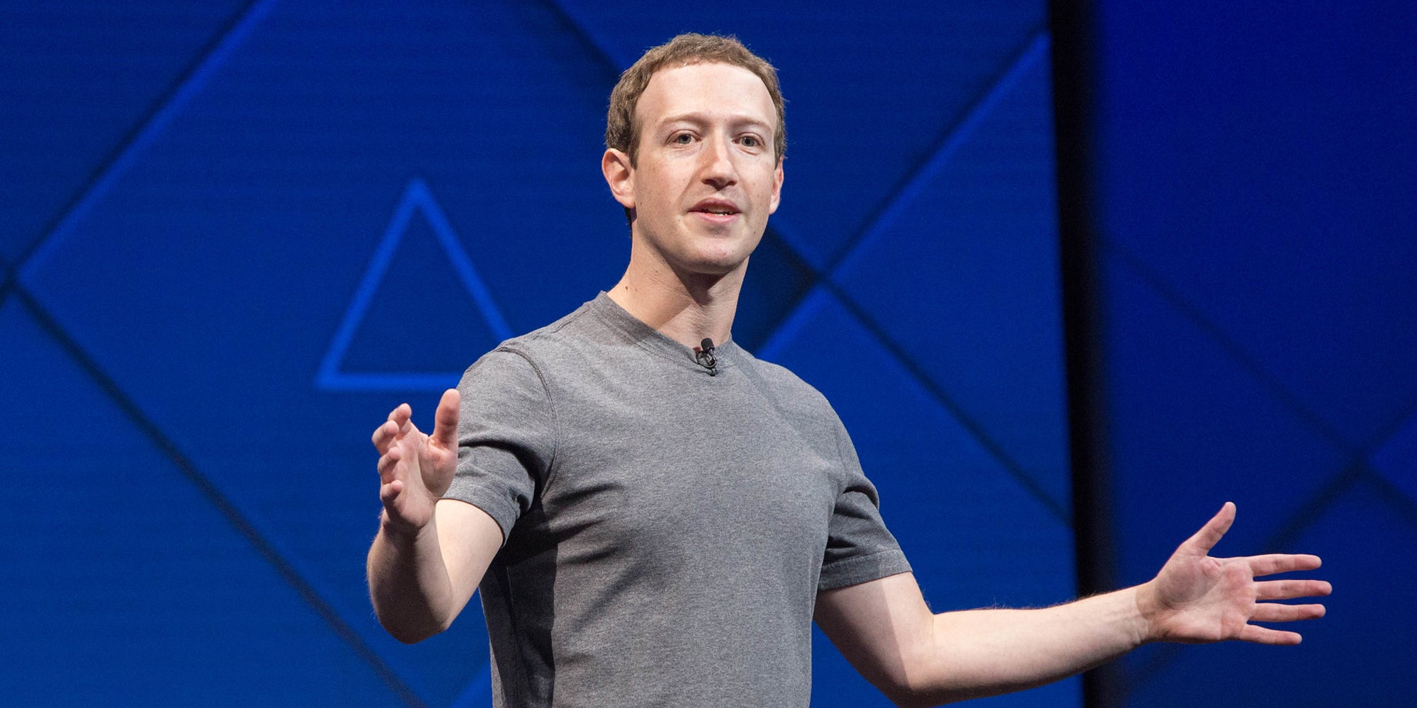 Facebook CEO Mark Zuckerberg giving a speech on a stage with his arms stretched out.