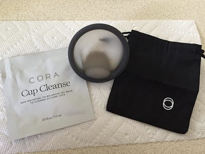 Cora disc on a paper towel in between its storage case and a cup cleansing solution.