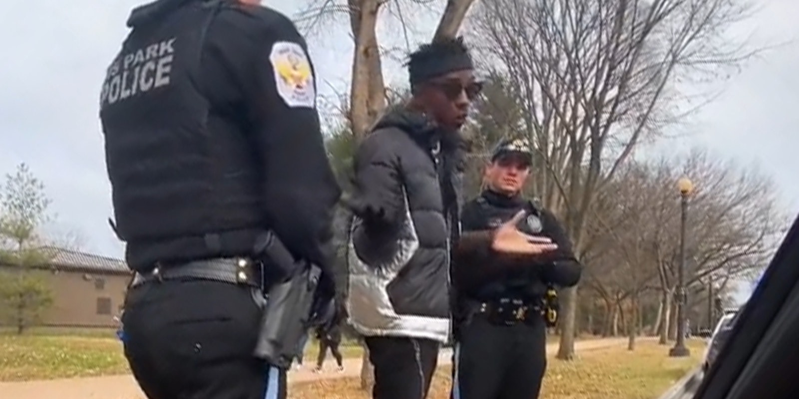 Two white police officers detain shrugging Black man.