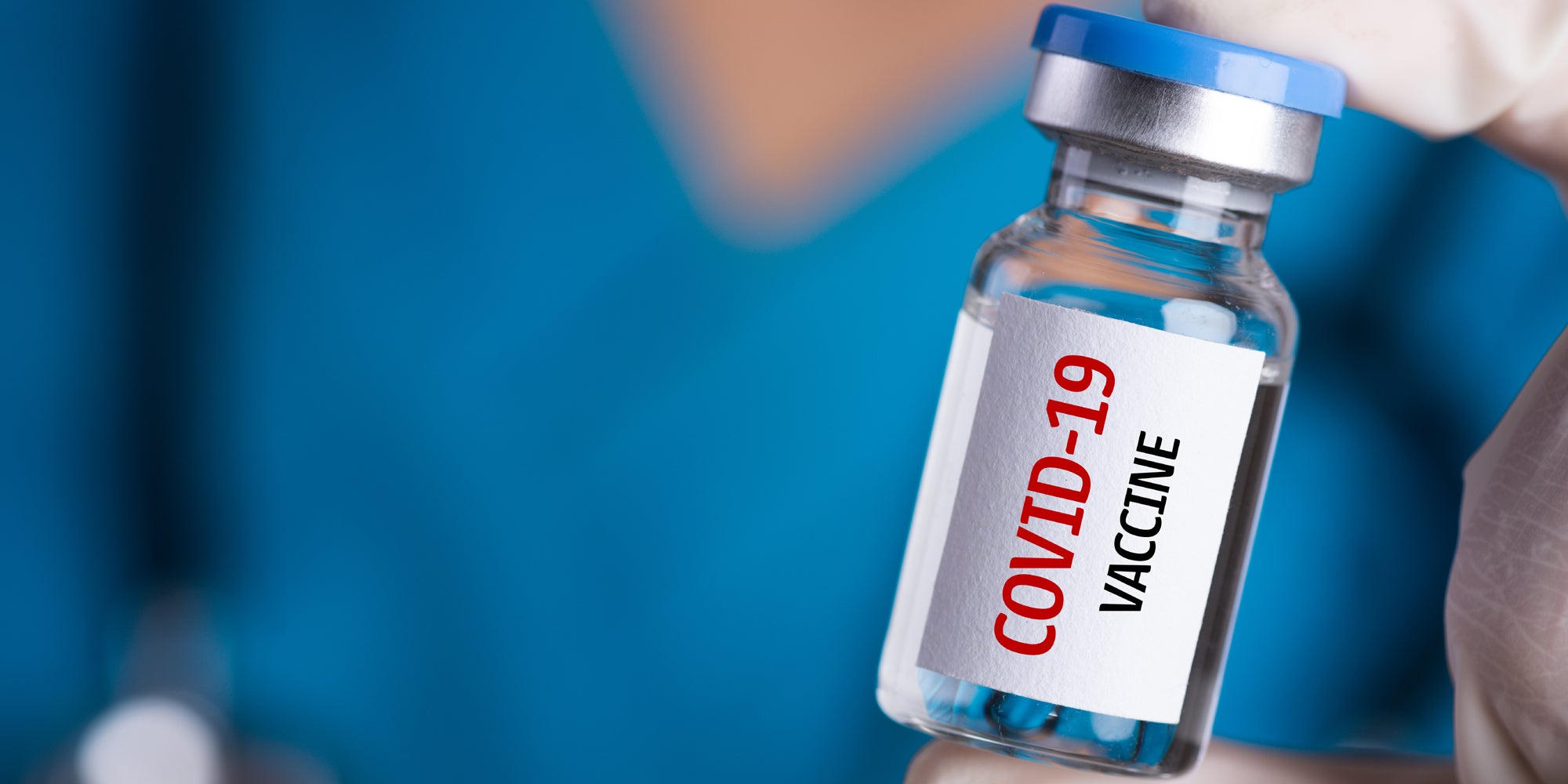 Female doctor with a stethoscope on shoulder holding syringe and COVID-19 vaccine.