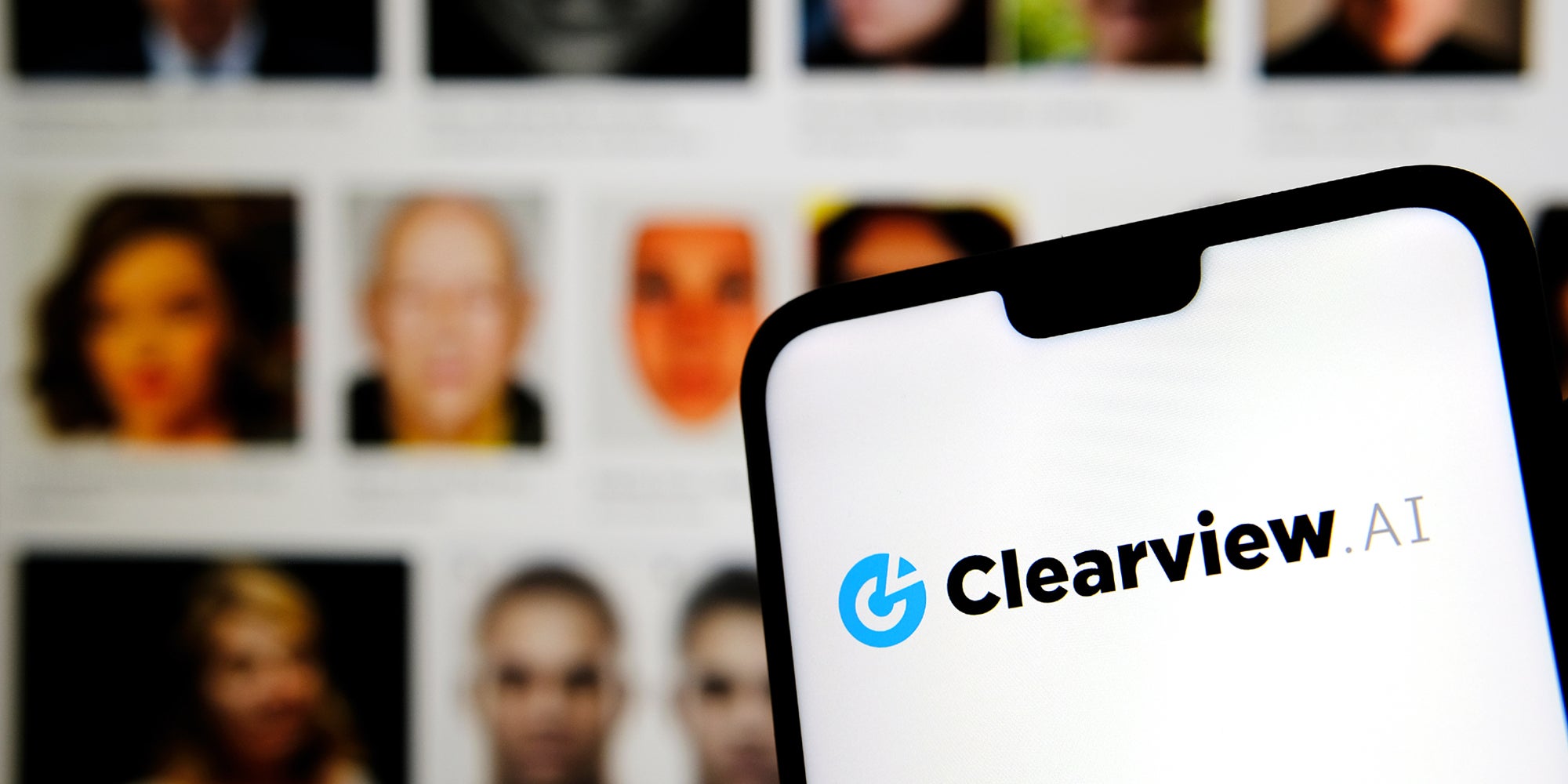A phone showing the Clearview AI logo on it. Behind it is a series of people's photos.
