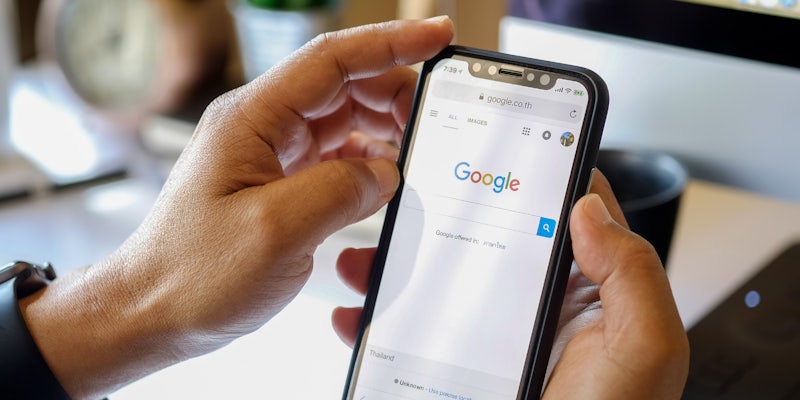 A person holding a smartphone with the Google homepage on it.