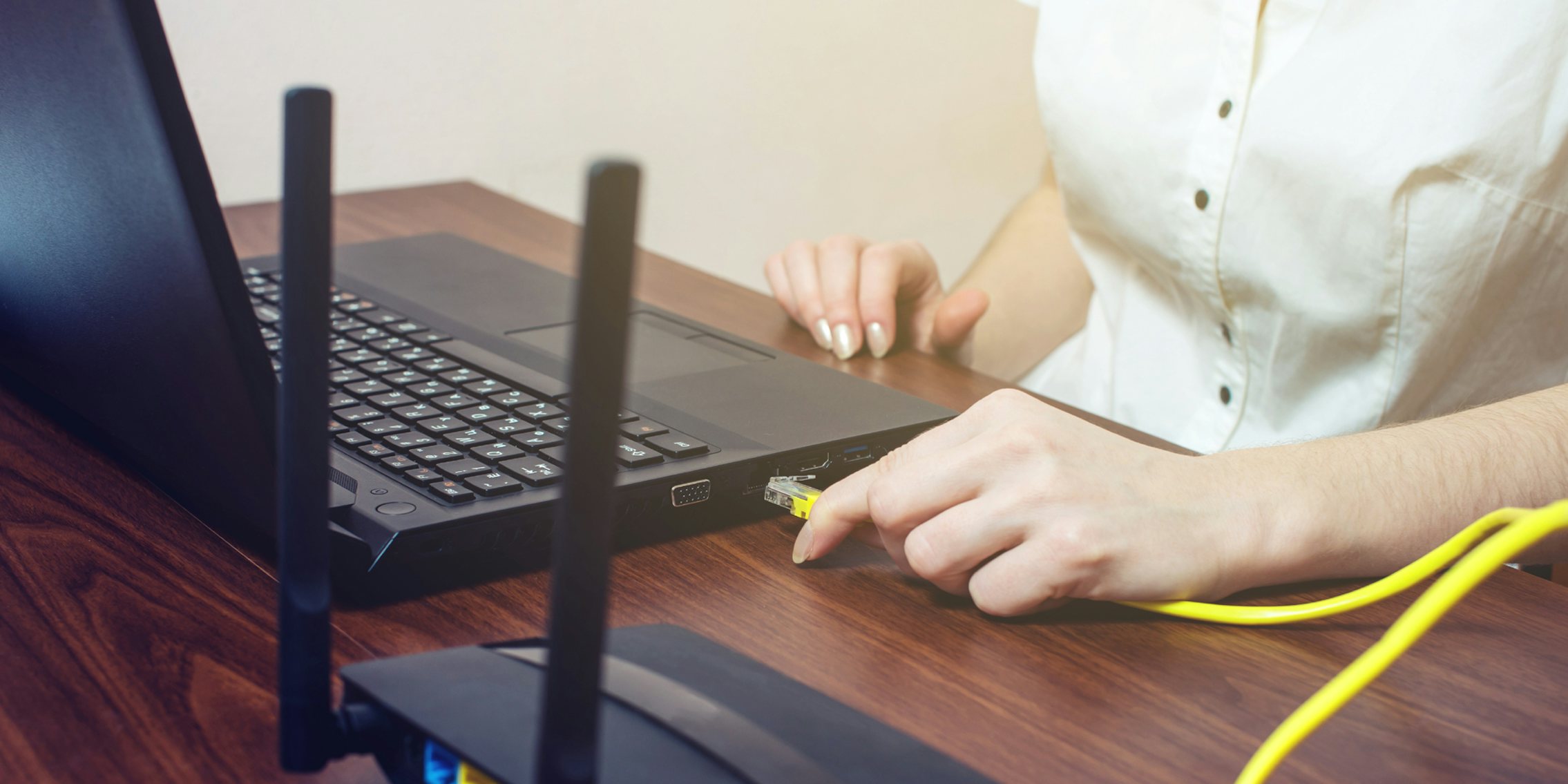 A woman connecting an ethernet cord into her laptop, attempting to get better broadband internet service.