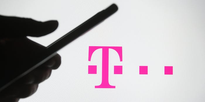 A person holding a smartphone in front of the T-Mobile logo.