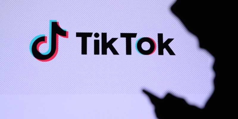 A person in shadows using a phone. Behind them is the TikTok logo.