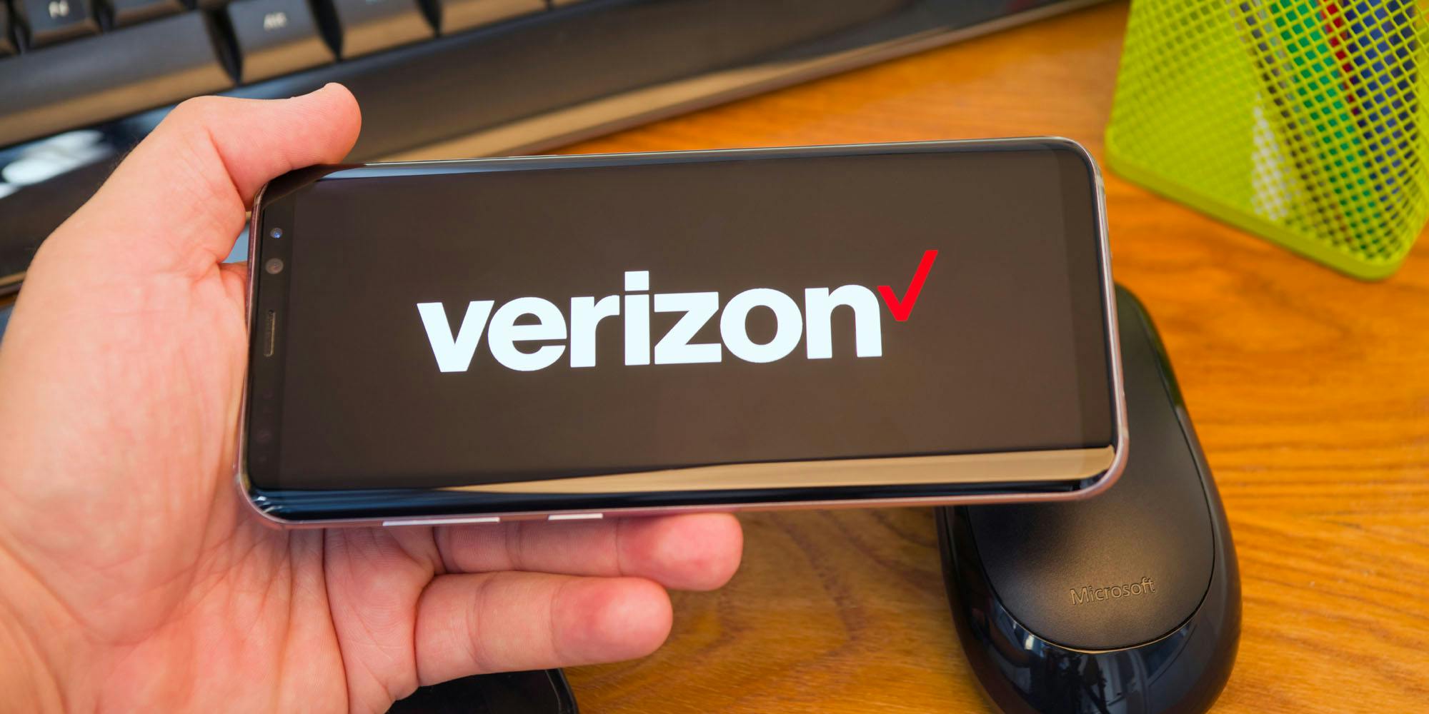 A person holds a smartphone with the Verizon logo on it.