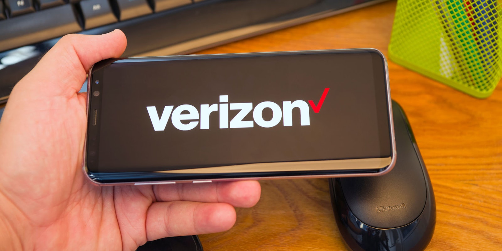 A person holds a smartphone with the Verizon logo on it.