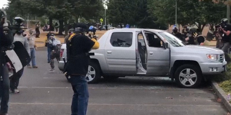 men in proud boys shirts fire paintball guns at man in truck as others attack him from the driver's side window