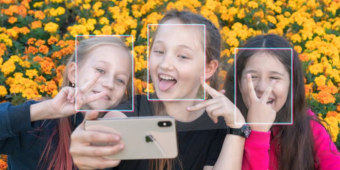 Three girls making faces at iPhone with facial recognition squares on their heads