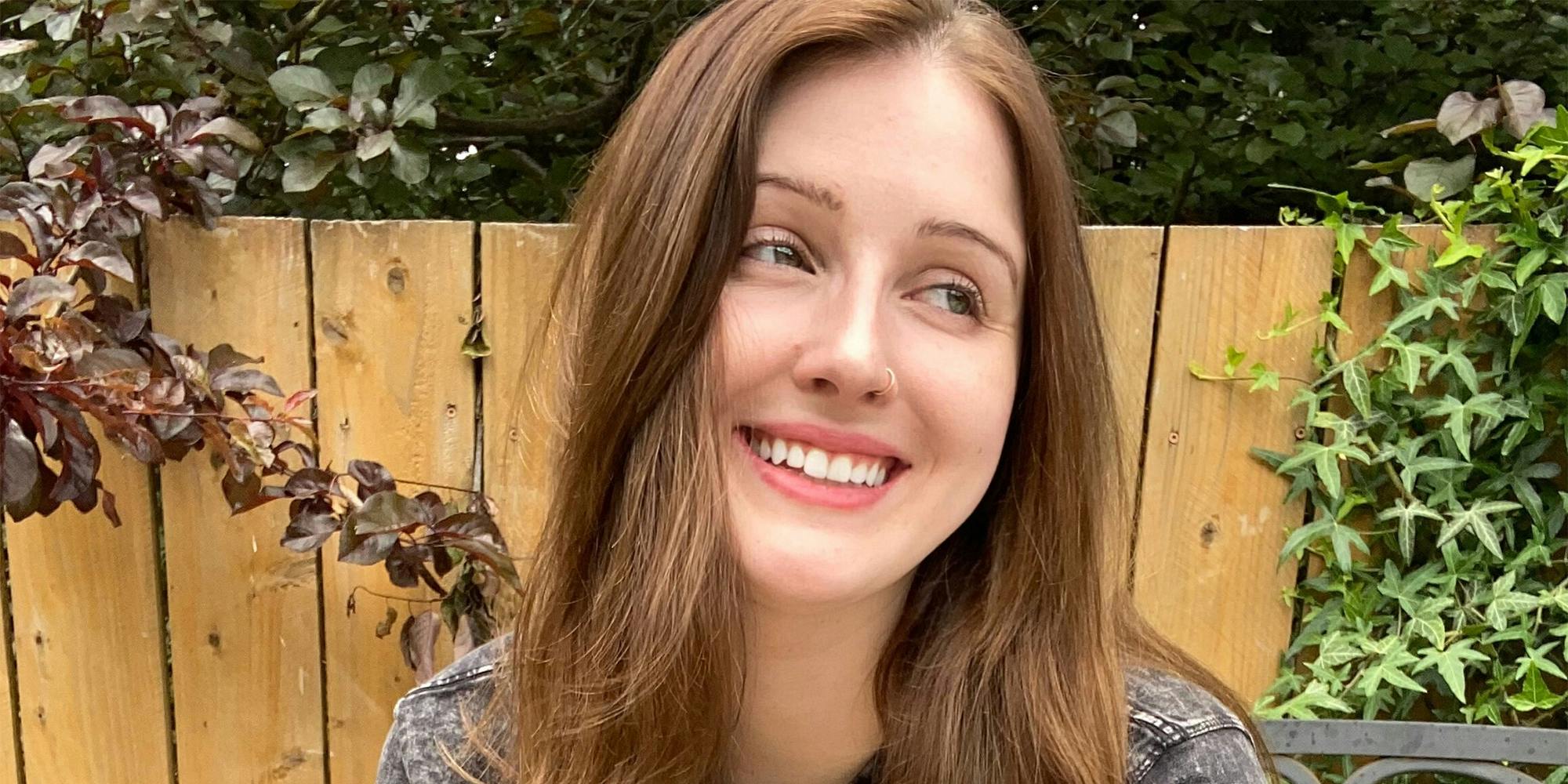 Smiling young woman in front of fence and plants