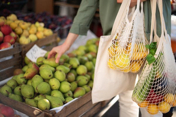 A shopper carrying ecofriendly resusable shopping bags gathers fresh fruit at the market