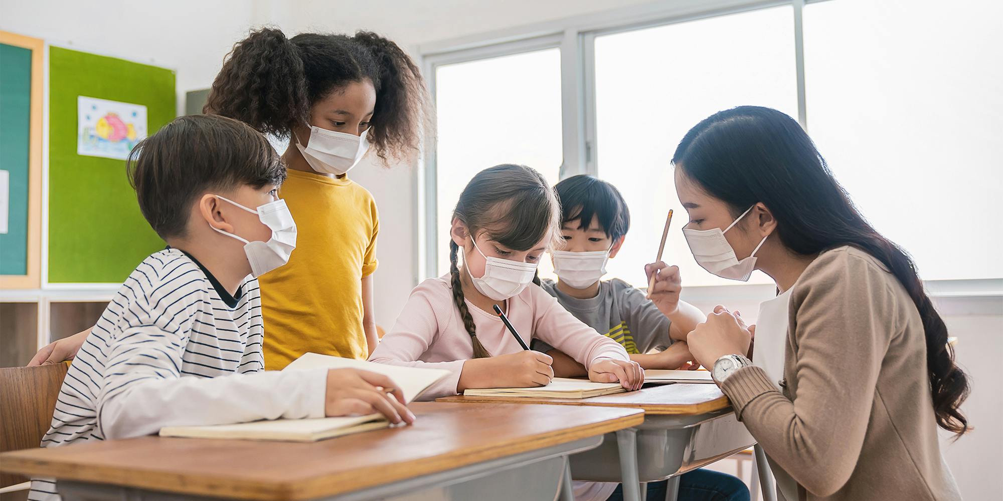 children at desks with teacher, all wearing facemasks